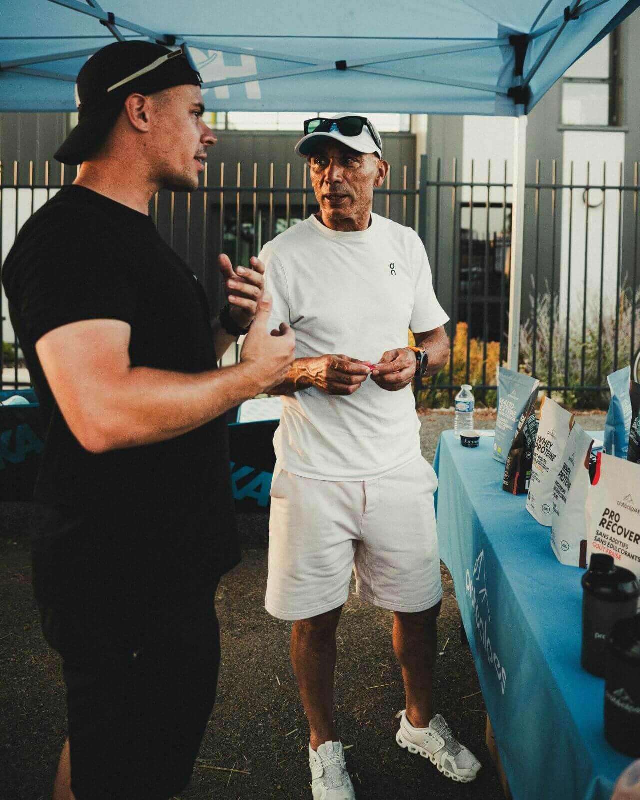 Deux hommes discutent près d'un stand Protéalpes, présentant des produits de nutrition sportive sans édulcorants ni additifs.