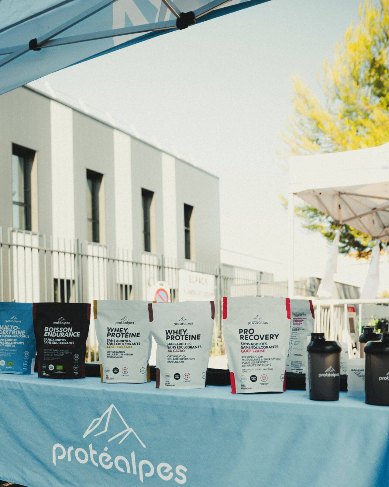 Stand Protéalpes avec produits de nutrition sportive sans édulcorants ni additifs exposés sur une table bleue.