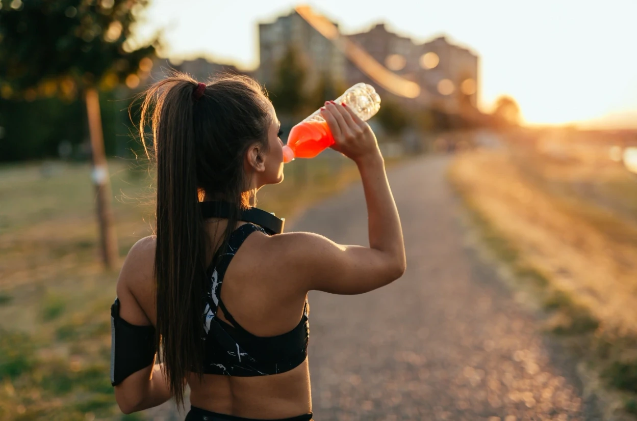 A sportswoman drinking a natural energy drink at sunset, a symbol of healthy nutrition from Protéalpes.