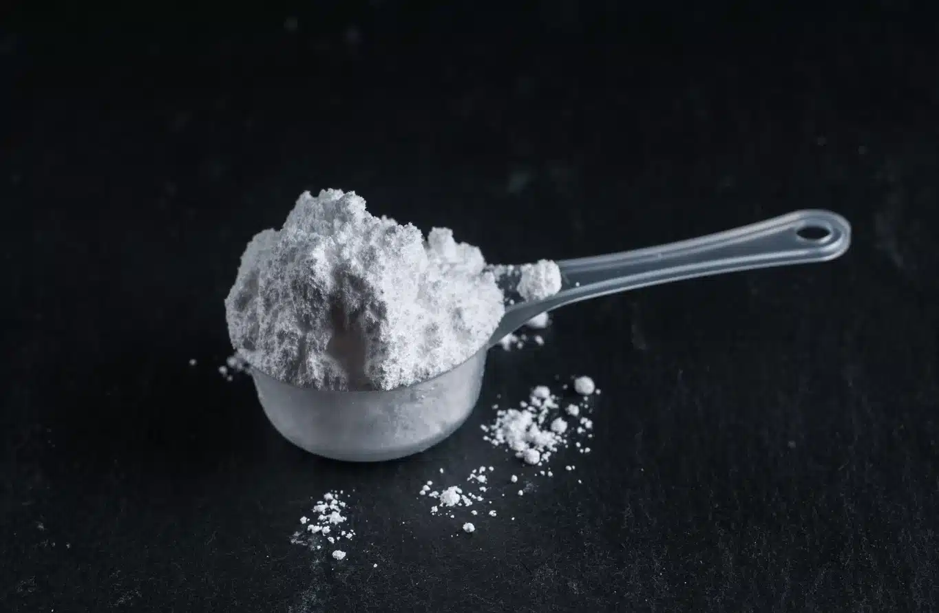 Löffel mit Protéalpes Sporternährungspulver, ohne Süßstoffe und Zusatzstoffe, auf schwarzem Hintergrund.