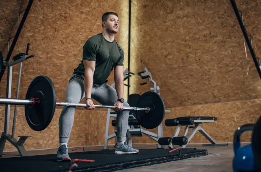 Athlet, der in einer Turnhalle eine olympische Hantelstange stemmt und damit Kraft und Ausdauer symbolisiert. Ernährung von Protéalpes.