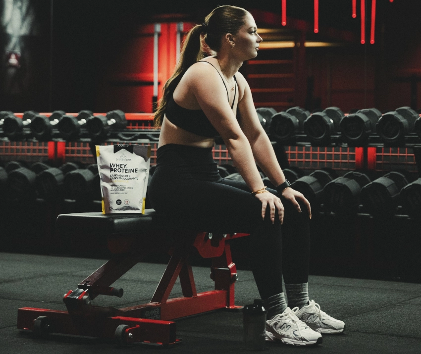 Athlète assise dans une salle de sport avec Whey Protéalpes, sans édulcorants ni additifs, pour une nutrition sportive pure.