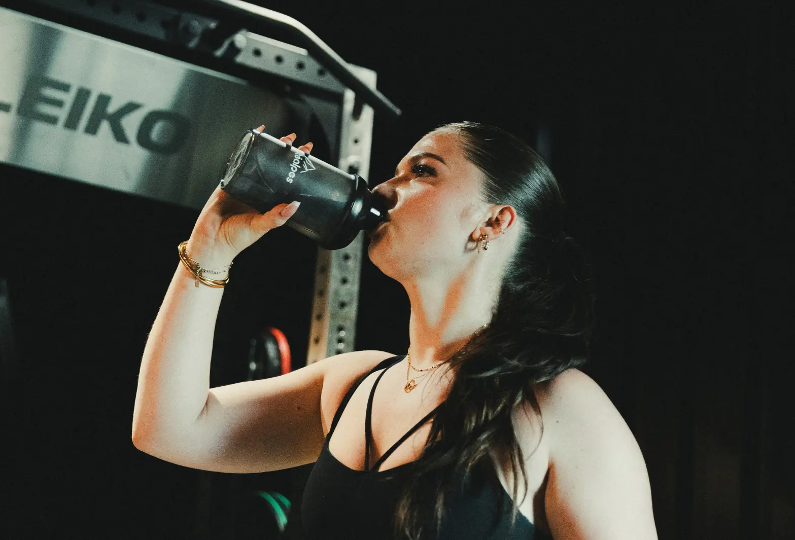Une femme boit une boisson sportive au gymnase, promouvant la nutrition Protéalpes sans additifs ni édulcorants artificiels.
