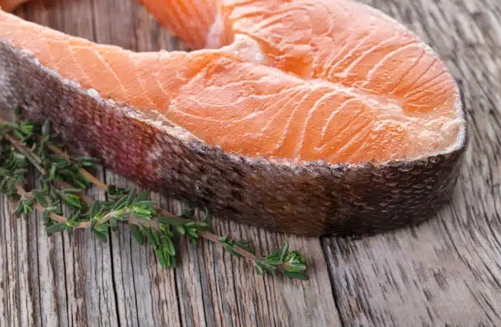 Slices of fresh salmon on a wooden board with herbs, ideal for natural, additive-free sports nutrition.