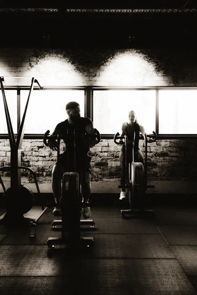 Two people work out on stationary bikes in a gym, symbolizing vitality and uncompromising endurance.