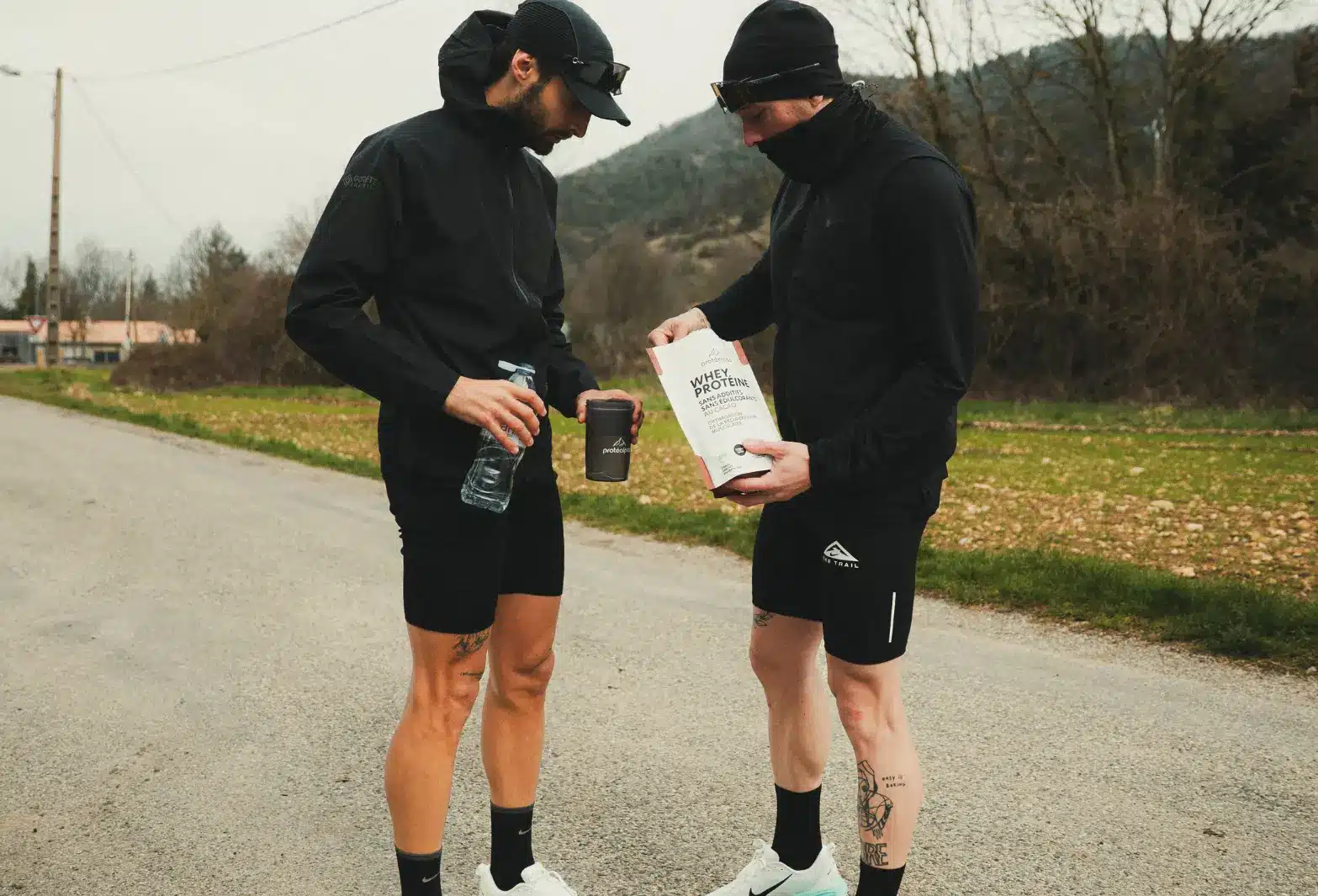 Deux sportifs discutent tout en tenant un shaker et un sachet de protéine sans édulcorants, en harmonie avec la nutrition Protéalpes.