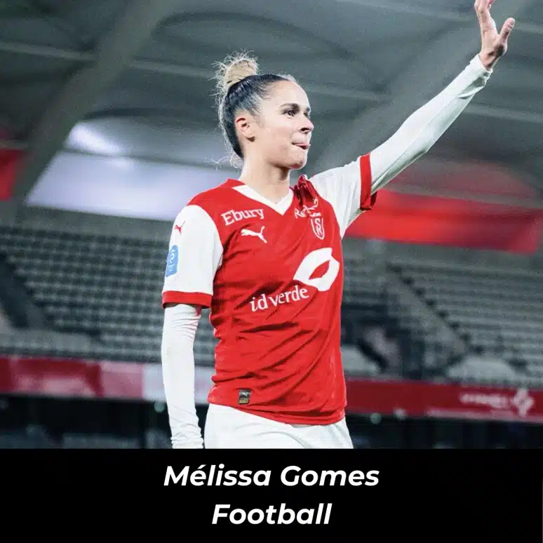 Joueuse de football en action dans un stade, levant la main, portant un maillot rouge et blanc.